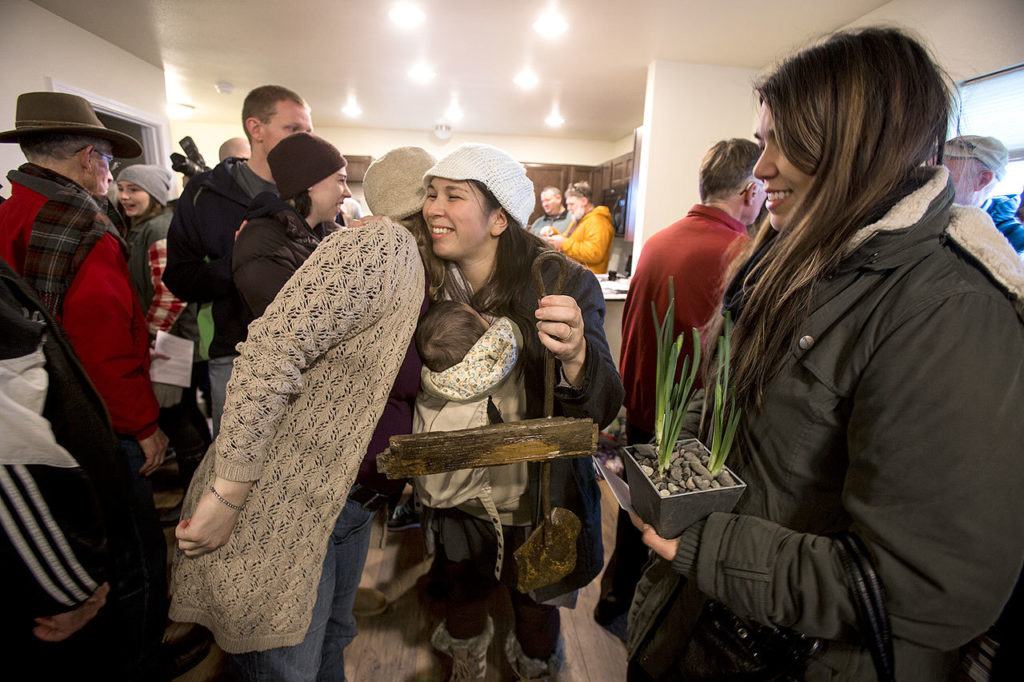 Sandy Flores, in white hat, hugs Sandi Olson, who made her a keys holder from items found in the previous home as they celebrate the Flores’ new home from Habitat for Humanity of Snohomish County on Saturday in Everett. The Flores and their three young children became the new owners of Phoenix II, a house in North Everett, to which they contributed more than 500 hours of sweat equity. (Andy Bronson / The Herald) 
