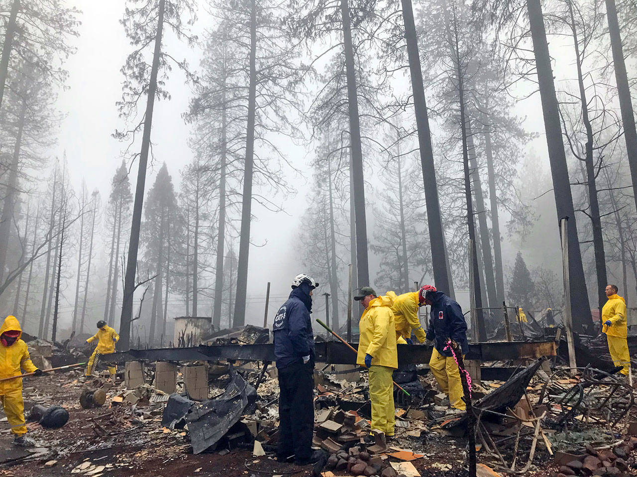 After a brief delay to let a downpour pass Nov. 23, volunteers resume their search for human remains at a mobile home park in Paradise, Calif. A massive wildfire that killed dozens of people and destroyed thousands of homes in Northern California has been fully contained after burning for more than two weeks, authorities said Sunday, Nov. 25. (AP Photo/Kathleen Ronayne, File)