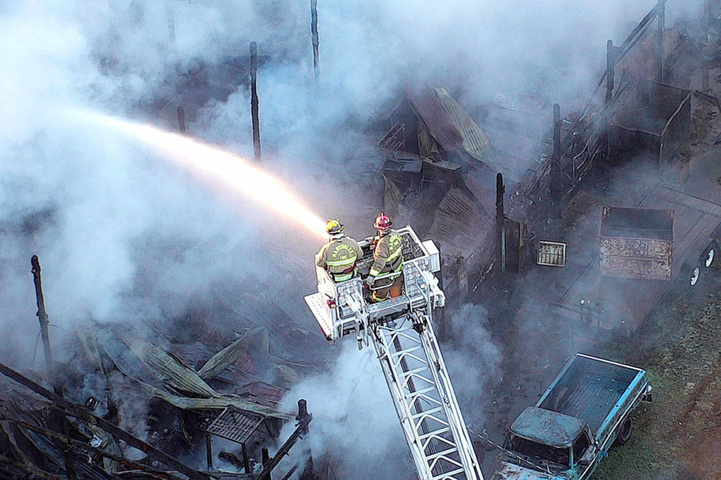 Firefighters work from a ladder to douse flames and hotspots early Tuesday morning at a pair of barns north of Lake Stevens. (Lake Stevens Fire)
