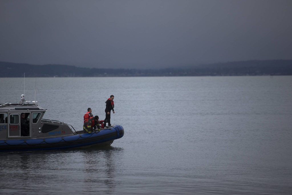 Everett rescue personnel peer over the sides of a boat in search of a man who was last seen swimming to shore after his inflatable boat capsized off the beach north of the Mukilteo ferry Wednesday. (Andy Bronson / The Herald)
