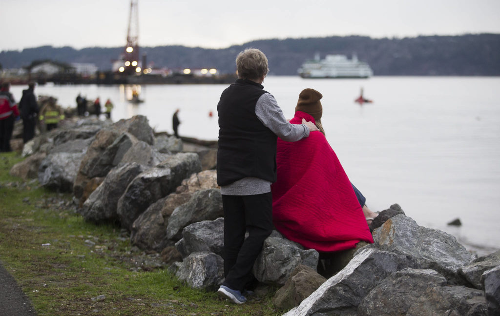 A witness is comforted as rescue personnel search for a man who was last seen swimming to shore after his inflatable boat capsized off the beach north of the Mukilteo ferry Wednesday. (Andy Bronson / The Herald)
