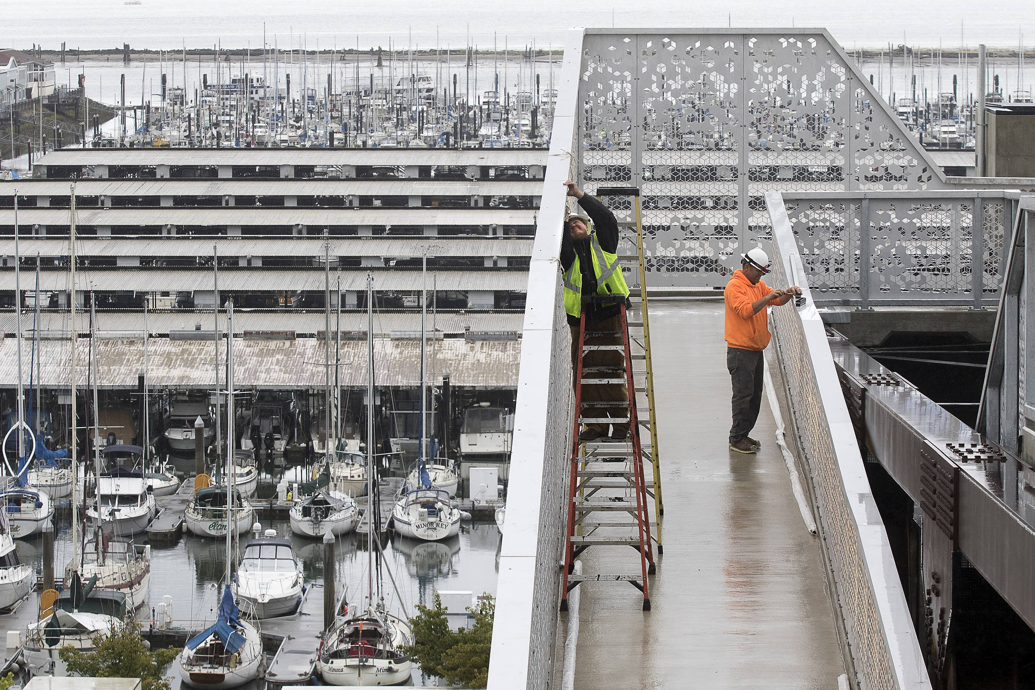 Electricians Alex Padilla (left) and Andy Graves work on installing lights at the Grand Avenue Park Bridge in Everett on July 1. Construction on the new $20 million utility span and walkway is set to wrap by the end of the month. (Andy Bronson / The Herald)