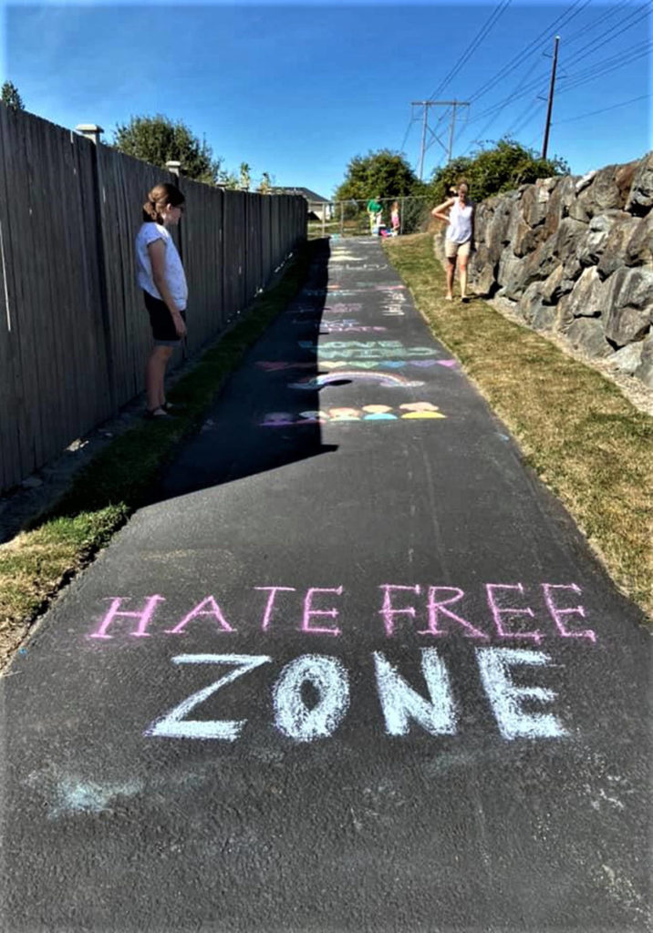 On a Lake Stevens neighborhood path, a young chalk artist looks on after Marnie Gray organized an “erase the hate” event in response to a racist slur and symbol found there earlier this month. Gray, a paraeducator, is also heading up Color Me Important, a charitable effort to supply teachers with classroom materials that represent students of color. (Marnie Gray photo)
