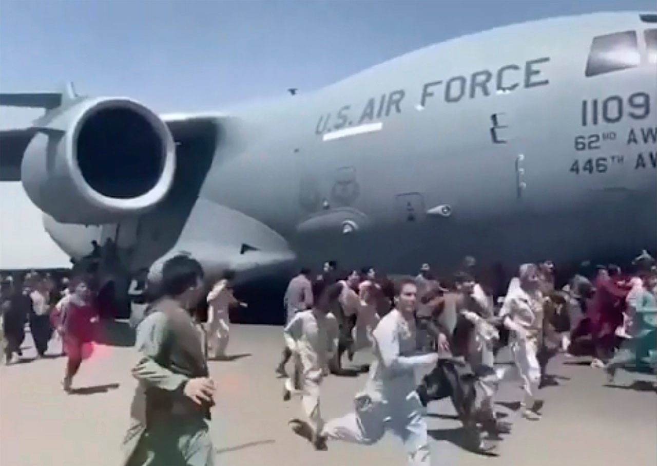 In an image from a video posted to Twitter, people run alongside a U.S. Air Force C-17 transport plane, reportedly based at Washington state’s Joint Base Lewis-McChorcd, as it moves down a runway of the international airport in Kabul, Afghanistan, Monday. Thousands of Afghans have rushed onto the tarmac of Kabul’s international airport, some so desperate to escape the Taliban capture of their country that they held onto an American military jet as it took off and fell to their death. (Associated Press)