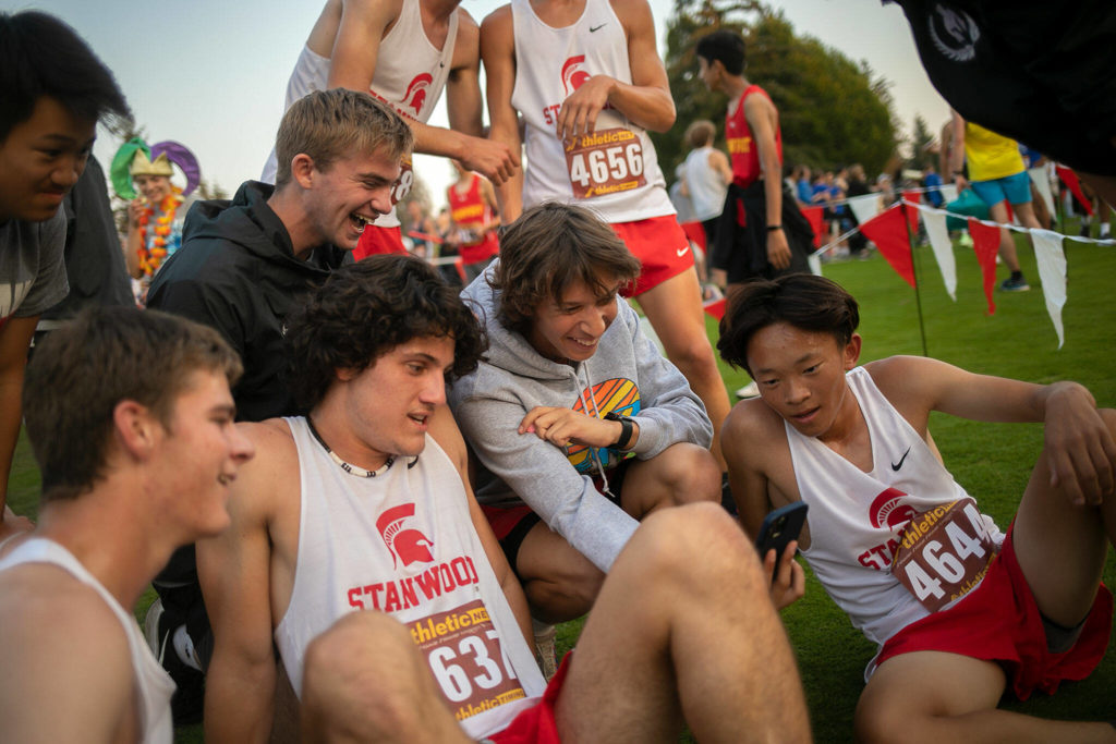 The Stanwood Boys cross country team watch a video during the Nike Twilight Cross Country Invitational on Saturday, Oct. 1, 2022, at Cedarcrest Golf Course in Marysville, Washington. (Ryan Berry / The Herald)

