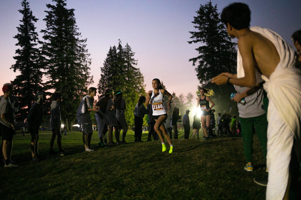 Fans cheer on one of the lead runners in the Girls 3A-4A 5K during the Nike Twilight Cross Country Invitational on Saturday, Oct. 1, 2022, at Cedarcrest Golf Course in Marysville, Washington. (Ryan Berry / The Herald)
