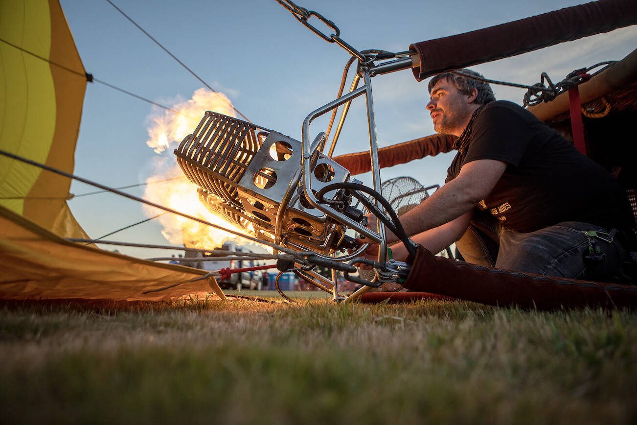 Erin Romaneschi, 33, fires up the burner and injects a hot air balloon with flame to heat the air inside during Kla Ha Ya Days at Harvey Field in Snohomish, Washington on Friday, July 14, 2023. (Annie Barker / The Herald)