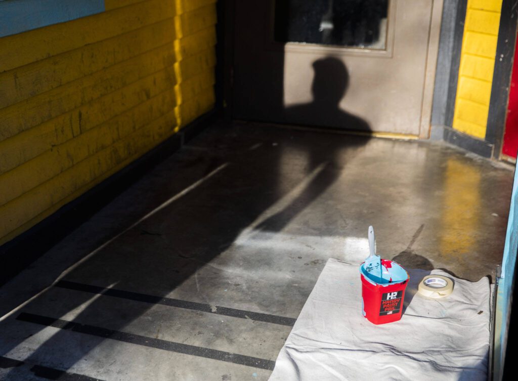 Reed casts a shadow int he entry to the Catalyst Cafe while painting the exterior on Thursday, Dec. 21, 2023 in Everett, Washington. (Olivia Vanni / The Herald)
