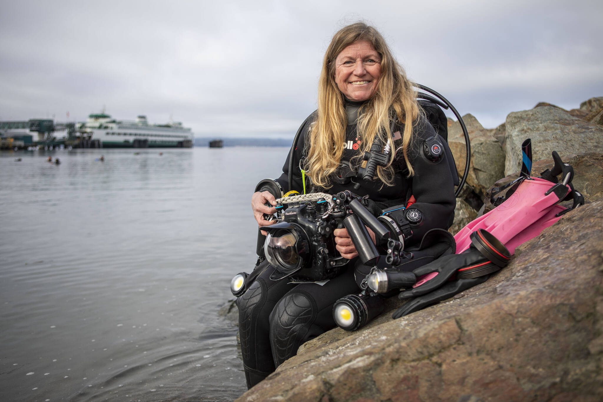 Annie Crawley poses for a photo with her scuba gear at Brackett’s Landing near the Port of Edmonds on Saturday, Feb. 3, 2024 in Edmonds, Washington. (Annie Barker / The Herald)