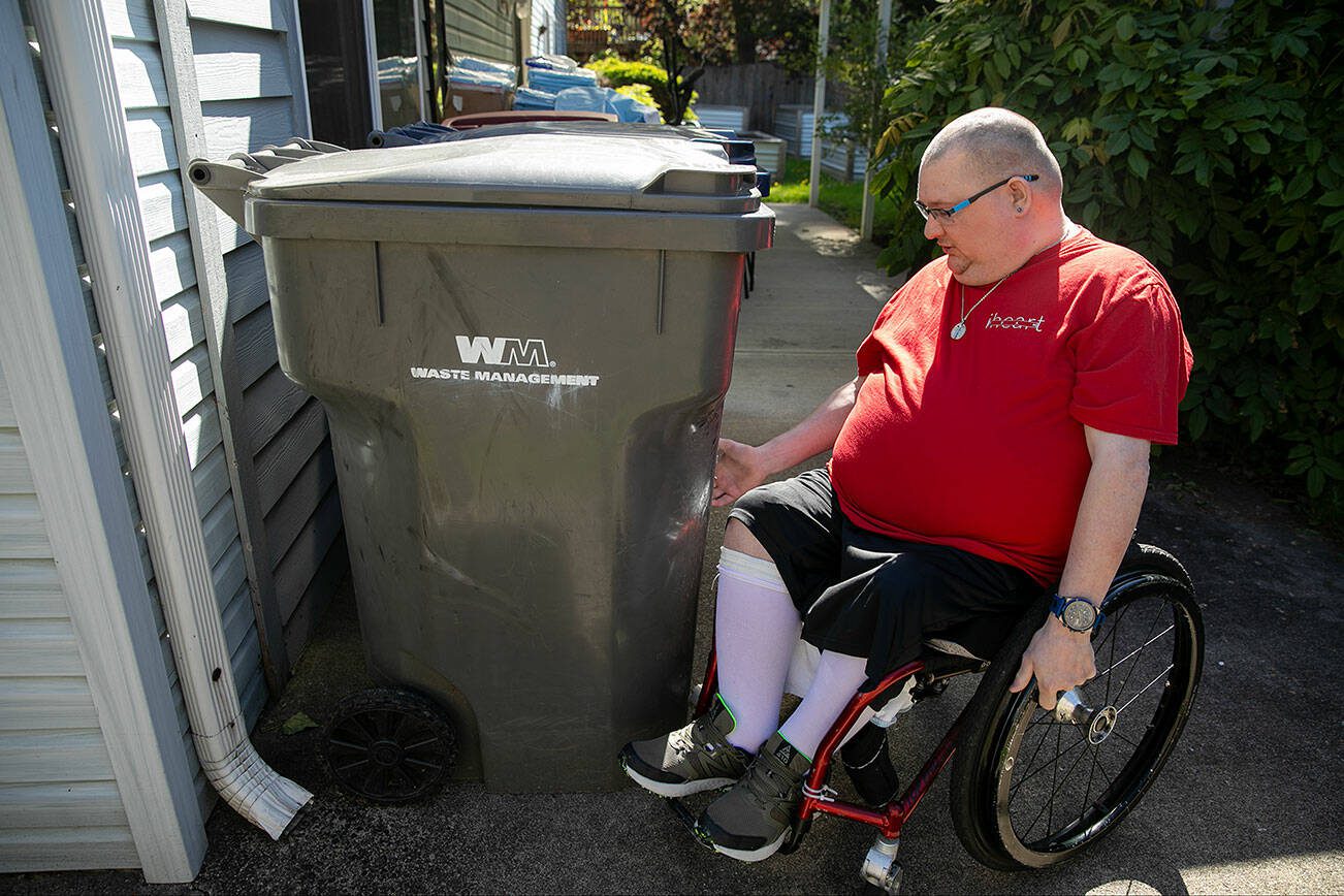 Ryan Carlson, 37, talks about how he takes garbage and recycling push carts to the curb while using his wheelchair at his group home on Friday, June 7, 2024, in Marysville, Washington. Carlson receives assistance from an aid to wrap a bungee cord around the container and then behind his legs in order to maintain control as he takes the bins to the curb. (Ryan Berry / The Herald)