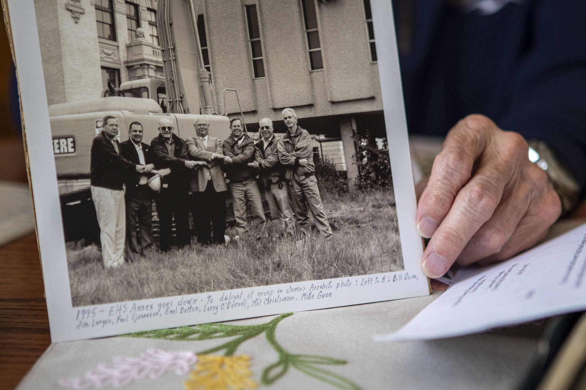 Lawrence E. O’Donnell holds a photograph of himself when he was a consultant and a part of a project removing “the annex” from Everett High School in 1995 at his brother Jack’s home in Everett, Washington on Wednesday, May 29, 2024. O’Donnell is third from the right. (Annie Barker / The Herald)