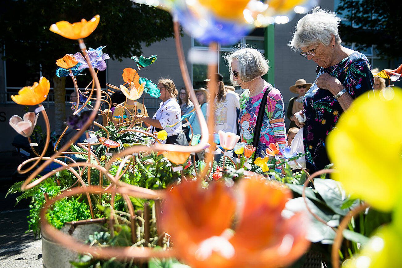 Nedra Vranish, left, and Karen Thordarson, right browse colorful glass flowers at Fuse4U during Sorticulture on Friday, June 7, 2024, in Everett, Washington. (Olivia Vanni / The Herald)