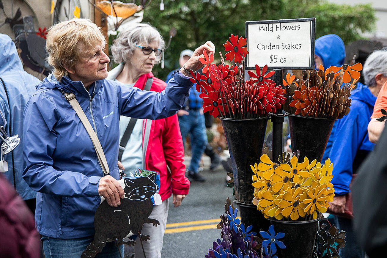 Dolly Hunnicutt holds onto a metal raccoon cutout while looking through metal wildflowers at the Freeborn Metal Art booth during the first day of Sorticulture on Friday, June 9, 2023 in Everett, Washington. (Olivia Vanni / The Herald)
