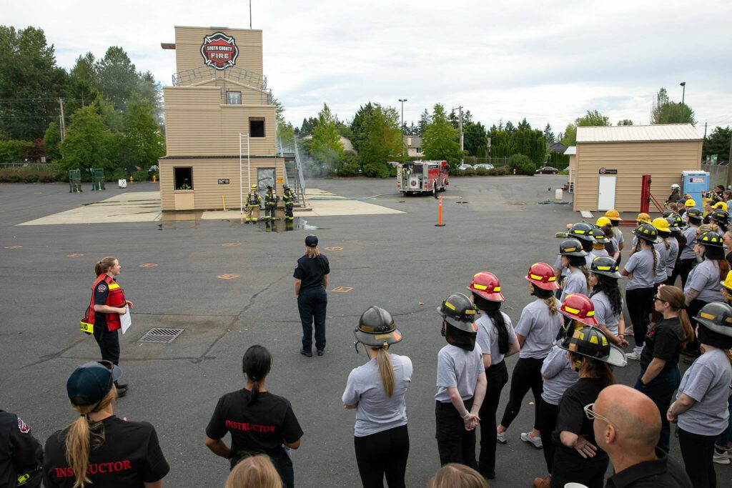 A group of about 30 participants and a number of instructors watch a simulated rescue during the Future Women in EMS/Fire Workshop on Saturday, June 22, 2024, at the South County Fire Training Center in Everett, Washington. (Ryan Berry / The Herald)
