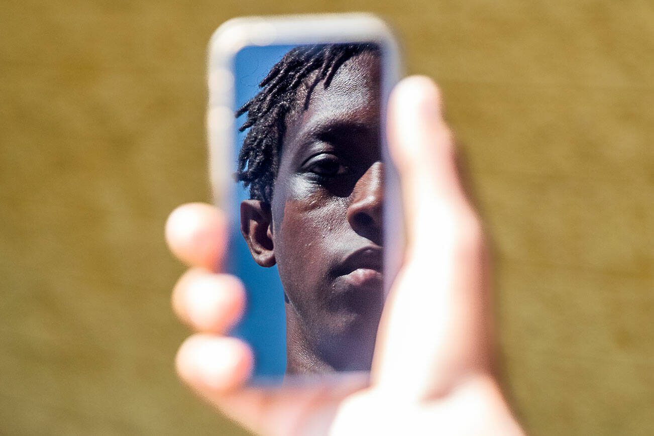 Jayden Hill, 15, an incoming sophomore at Monroe High School is reflected in the screen of a cellphone on Wednesday, July 10, 2024 in Monroe, Washington. (Olivia Vanni / The Herald)