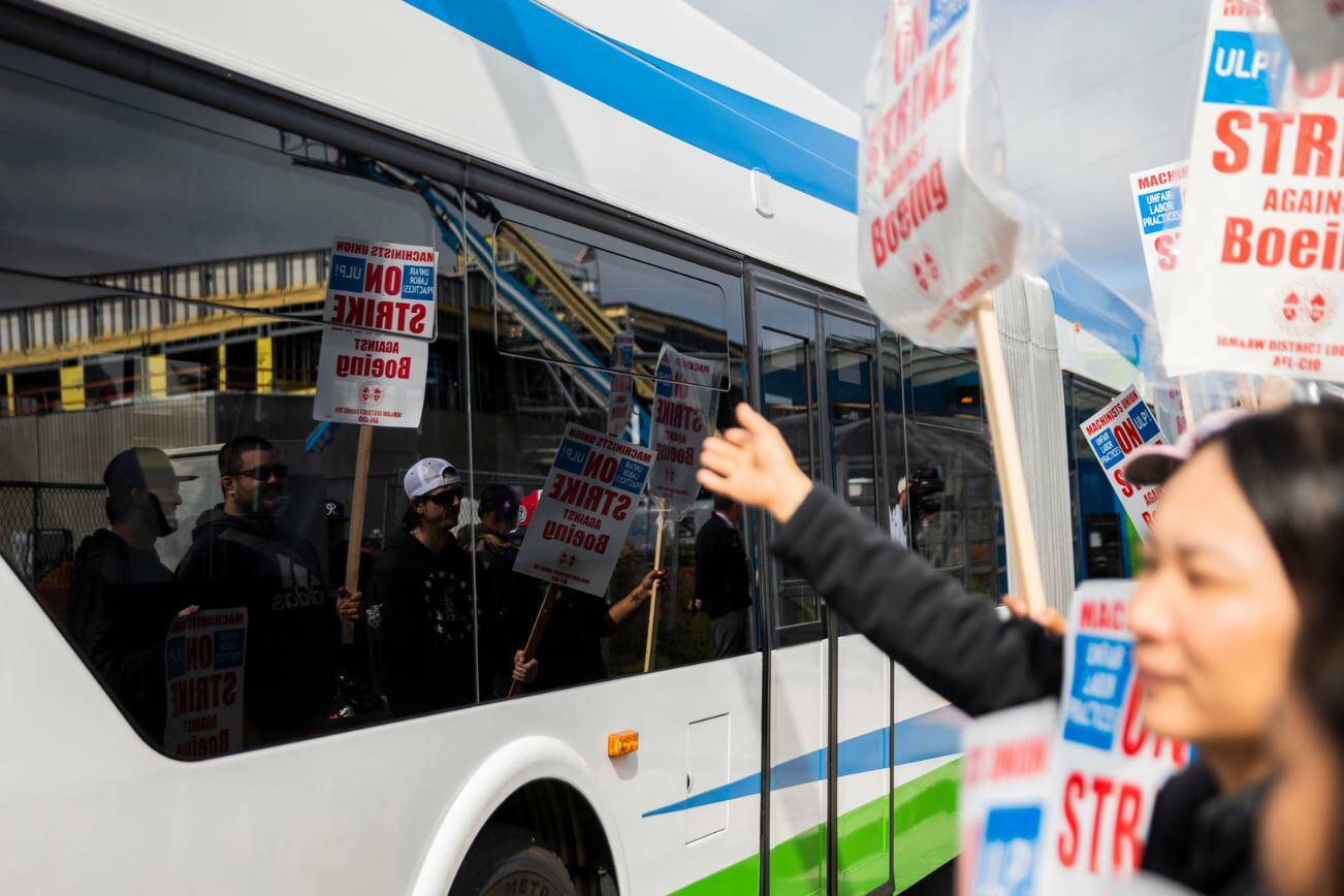 Striking Boeing workers are reflected in the windows of a bus as it drives along Airport Road on Monday, Sept. 16, 2024 in Everett, Washington. (Olivia Vanni / The Herald)