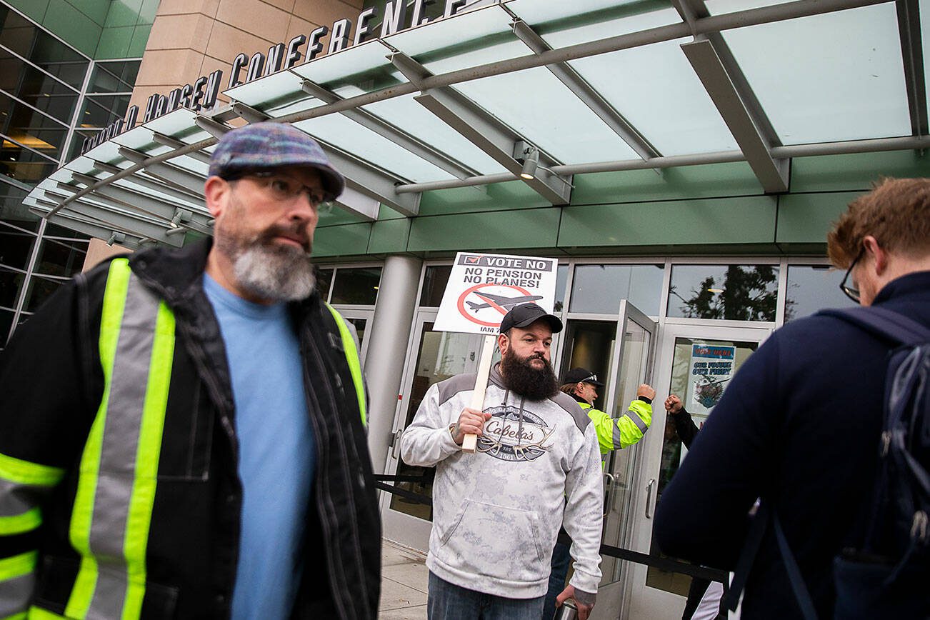 Matt Farnum, center, a machine repair mechanic at Boeing for 14 years, stands outside of Angel of the Winds Arena holding a “vote no” sign as people file inside to vote on the proposed contract on Wednesday in Everett. (Olivia Vanni / The Herald)