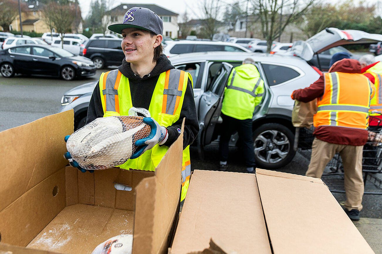 Lucas Rudzinski, 14, smiles as he picks up a frozen turkey to load into one of the hundreds of cars lined up to receive food from the Mukilteo Food Bank on Monday, Nov. 25, 2024 in Mukilteo, Washington. (Olivia Vanni / The Herald)